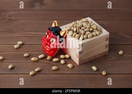parched soy beans in measuring box with demon mask isolated on wooden table Stock Photo