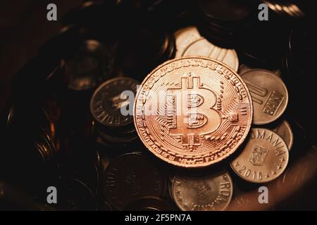 Shallow depth of field (selective focus) image with a Bitcoin metal coin on top of other metal coins (Romanian RON) - cryptocurrency concept. Stock Photo