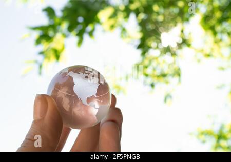 Crystal globe in the hand of a man against a background of blue sky and green foliage. Earth protection concept. nature protection Stock Photo