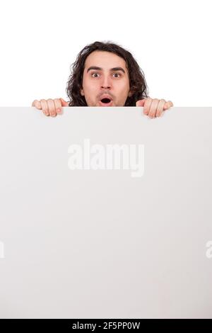 Positively surprised young man, long curly hair style, staring with big eyes and mouth open, behind a big, blank announcement banner. Amazed guy, asto Stock Photo