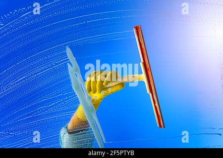 Hand in yellow glove cleaning window glass with squeegee on a sunny summer day. Stock Photo