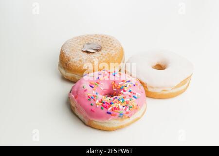 Three fresh, colourful ring doughnuts isolated on a plain white surface and background. Stock Photo