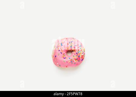 Overhead flat lay view of  fresh, ring doughnut with pink frosting and colourful sprinkles isolated on a plain white surface and background. Stock Photo