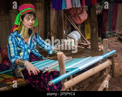 Karen long neck woman wearing traditional brass rings and weaving a shawl in a hill tribe village near Chiang Mai, Thailand. Stock Photo