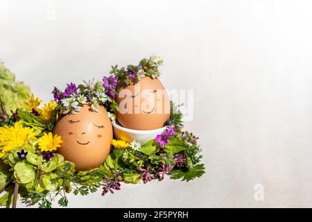 Easter and Springtime concept. Two eggs with a smiling face and a flower garlands enjoying Springtime sun on a bed of elm seeds and wildflowers Stock Photo
