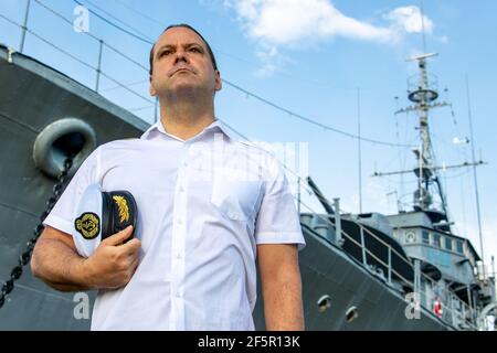 The sailor officer in white uniform stands beside battleship. Stock Photo