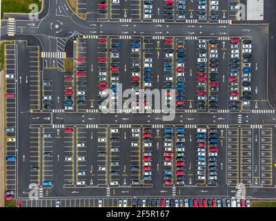 Busy large modern carpark with symmetrical roads rows of parking bays lots of symmetry and colours aerial view from drone up above looking down tarmac Stock Photo