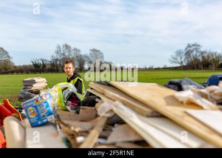 A young adult male builder wearing a high visibility vest throwing rubbish into a skip Stock Photo