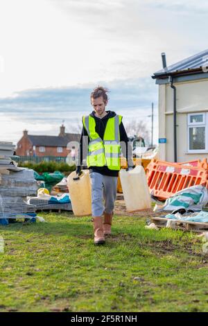 A young adult male builder wearing a high visibility vest carrying to storage tanks while on a building site Stock Photo
