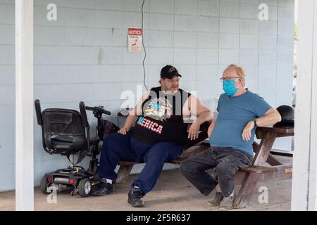 Two men Sitting at talking at a small town park, one with a mask and one without Stock Photo