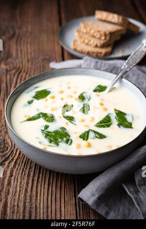 Creamy chickpea and garlic soup with spinach and mashed potatoes, served with whole grain bread on rustic wooden background Stock Photo