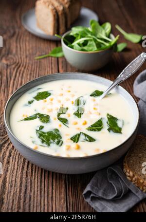 Creamy chickpea and garlic soup with spinach and mashed potatoes, served with whole grain bread on rustic wooden background Stock Photo