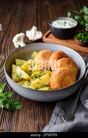 Fried cauliflower and cheese croquettes with boiled potatoes and sour cream dip on rustic wooden background Stock Photo