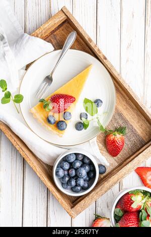 Cream cheese tart slices with lemon curd topping, served with fresh blueberries and strawberries on white rustic background Stock Photo