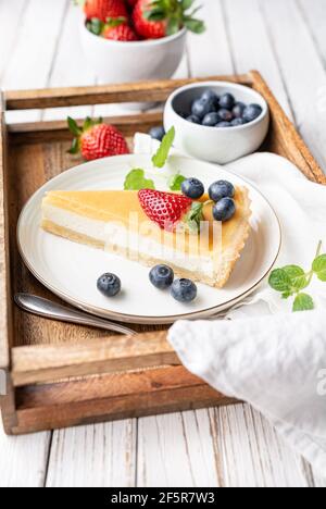 Cream cheese tart slices with lemon curd topping, served with fresh blueberries and strawberries on white rustic background Stock Photo