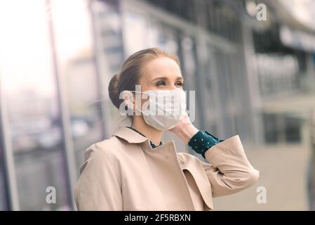 Confident woman wearing face mask and talking with somebody on mobile phone while walking in front of business center during coronavirus pandemic. Stock Photo