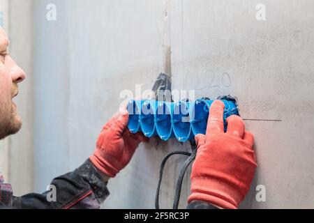 The electrician inserts the plastic box directly into the outlet holes. Close-up Stock Photo