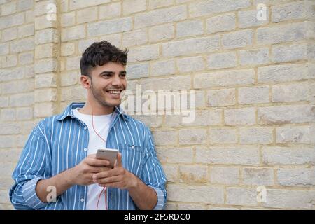 Заголовок	 Handsome asian man using mobile phone, chatting, communication, looking at copy space. Smiling Indian hipster listening music outdoors Stock Photo