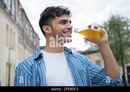 Young stylish Indian man holding glass with drinks, walking on the street, Portrait of happy asian guy wearing casual clothes, drinking juice outdoors Stock Photo