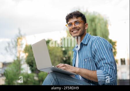 Portrait of handsome Indian copywriter using laptop computer, typing, working freelance project online. Asian student studying, learning language Stock Photo