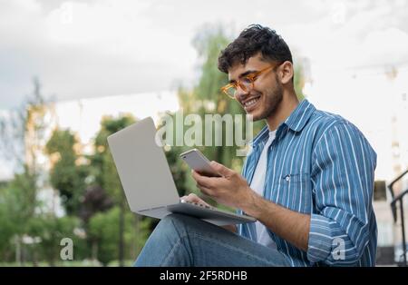 Indian man using laptop computer, mobile phone, working freelance project online. Successful business. Asian student studying, online education Stock Photo