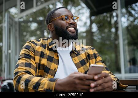 Smiling handsome African American man using mobile phone, shopping online. Portrait of young guy wearing stylish eyeglasses holding smartphone Stock Photo