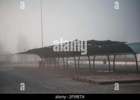 View of a foggy empty covered car parking area inside of a typical filling station zone of Portugal; a parking lot with an overhang on a grey misty mo Stock Photo