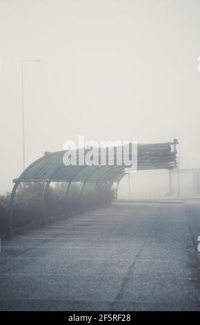 A vertical foggy scenery with a morning view of a parking on the territory of a filling station with a curved metal roof of a canopy against the rain Stock Photo