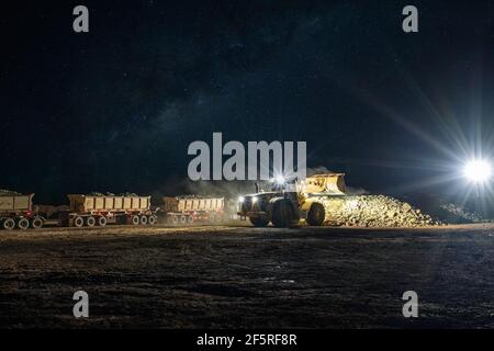 Open pit mining operation at night with drill rigs, dump trucks and loaders operating under floodlights. Stock Photo