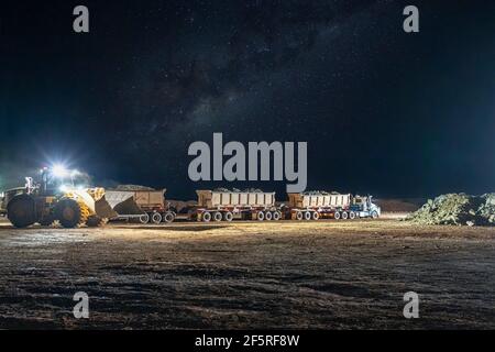 Open pit mining operation at night with drill rigs, dump trucks and loaders operating under floodlights. Stock Photo