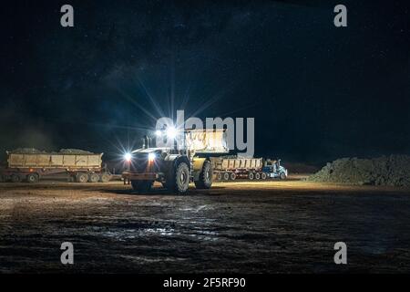 Open pit mining operation at night with drill rigs, dump trucks and loaders operating under floodlights. Stock Photo