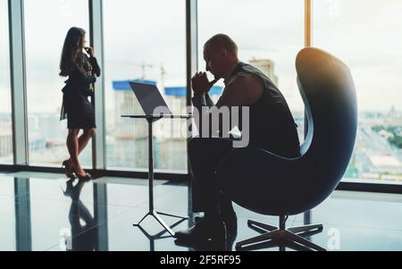 Silhouettes of two entrepreneurs on the top floor of a luxury business high-rise, near the window with a construction site outside: a pensive business Stock Photo