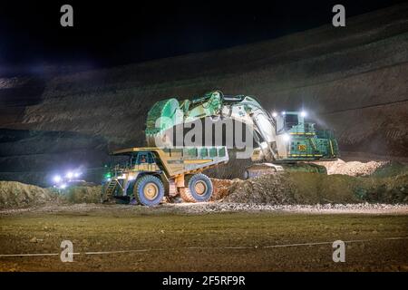 Open pit mining operation at night with drill rigs, dump trucks and loaders operating under floodlights. Stock Photo