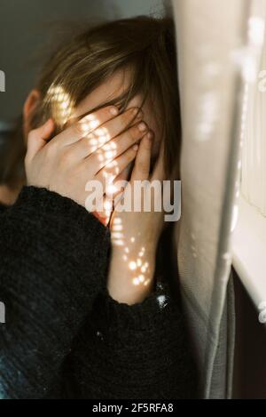 Little boy holding his eyes shut in front of bright window light