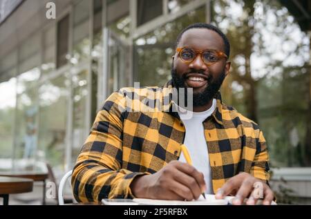 Smiling university student studying, exam preparation, taking notes. Education concept. African American business man writing on notebook, working Stock Photo