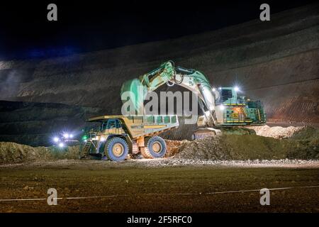 Open pit mining operation at night with drill rigs, dump trucks and loaders operating under floodlights. Stock Photo