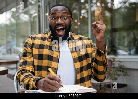 Portrait of emotional African American student studying, learning language, holding finger up, having creative idea Stock Photo