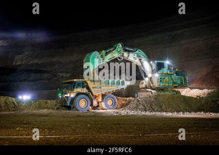 Open pit mining operation at night with drill rigs, dump trucks and loaders operating under floodlights. Stock Photo