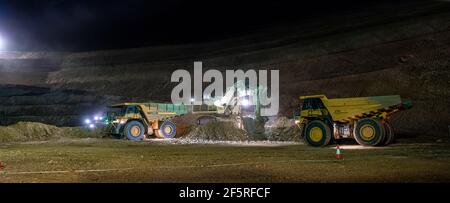 Open pit mining operation at night with drill rigs, dump trucks and loaders operating under floodlights. Stock Photo