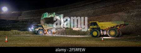 Open pit mining operation at night with drill rigs, dump trucks and loaders operating under floodlights. Stock Photo