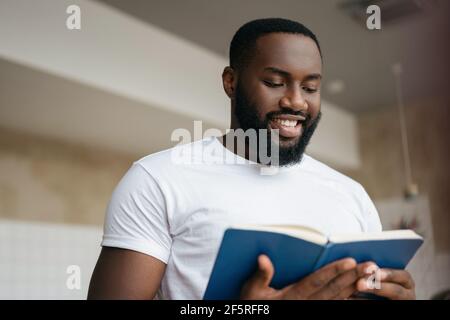 Portrait of handsome African American man reading book, exam preparation. University student studying, learning language, education concept Stock Photo