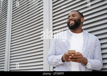 Young smiling African American man using mobile application for online shopping on black Friday. Portrait of handsome businessman holding cellphone Stock Photo
