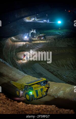 Open pit mining operation at night with drill rigs, dump trucks and loaders operating under floodlights. Stock Photo