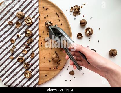 Young woman is cracking walnut on a wooden board and white background. Stock Photo