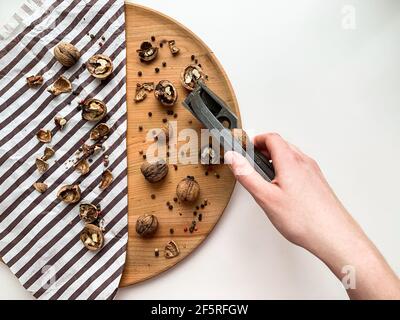 Woman cracking walnuts on a wooden board, white copy space background. Stock Photo