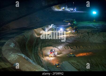 Open pit mining operation at night with drill rigs, dump trucks and loaders operating under floodlights. Stock Photo