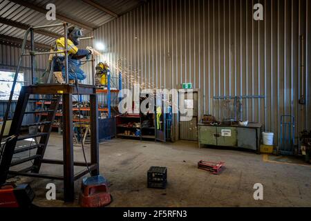 Boilermaker in protective clothing using grinder on metal stairway Stock Photo