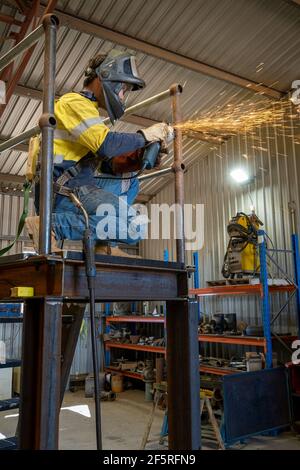 Boilermaker in protective clothing using grinder on metal stairway Stock Photo