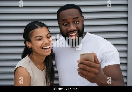 Emotional African American man and woman holding mobile phone, shopping online. Young happy couple communication online, video call concept Stock Photo