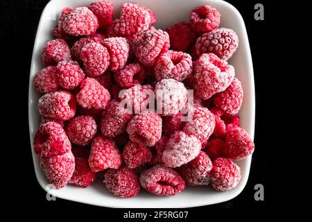 frozen ripe raspberries in a white deep plate on a black background Stock Photo